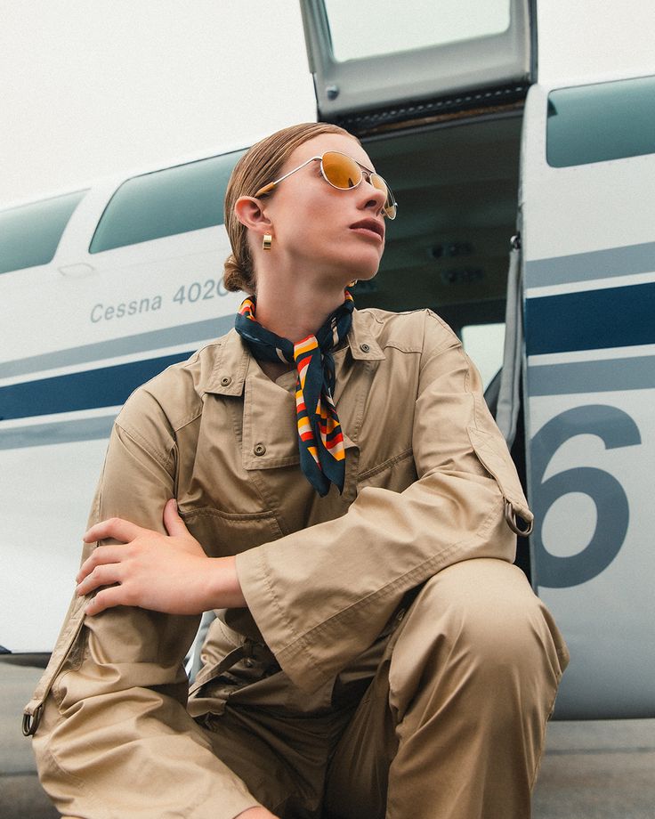 Mujer con gafas Aviator Randolph doradas junto a avioneta, en estilo aviador vintage