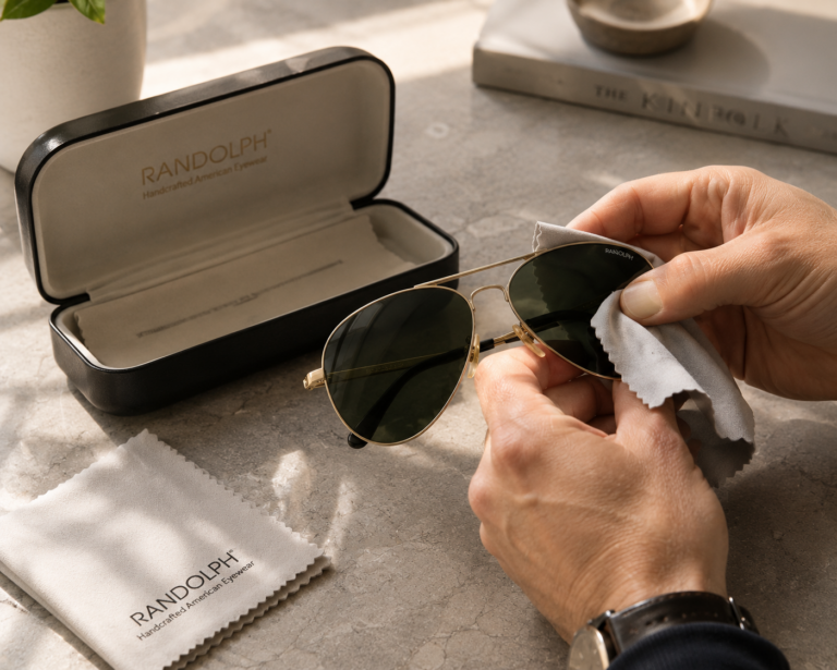 Persona limpiando unas gafas de sol premium con una gamuza de microfibra sobre una superficie elegante.